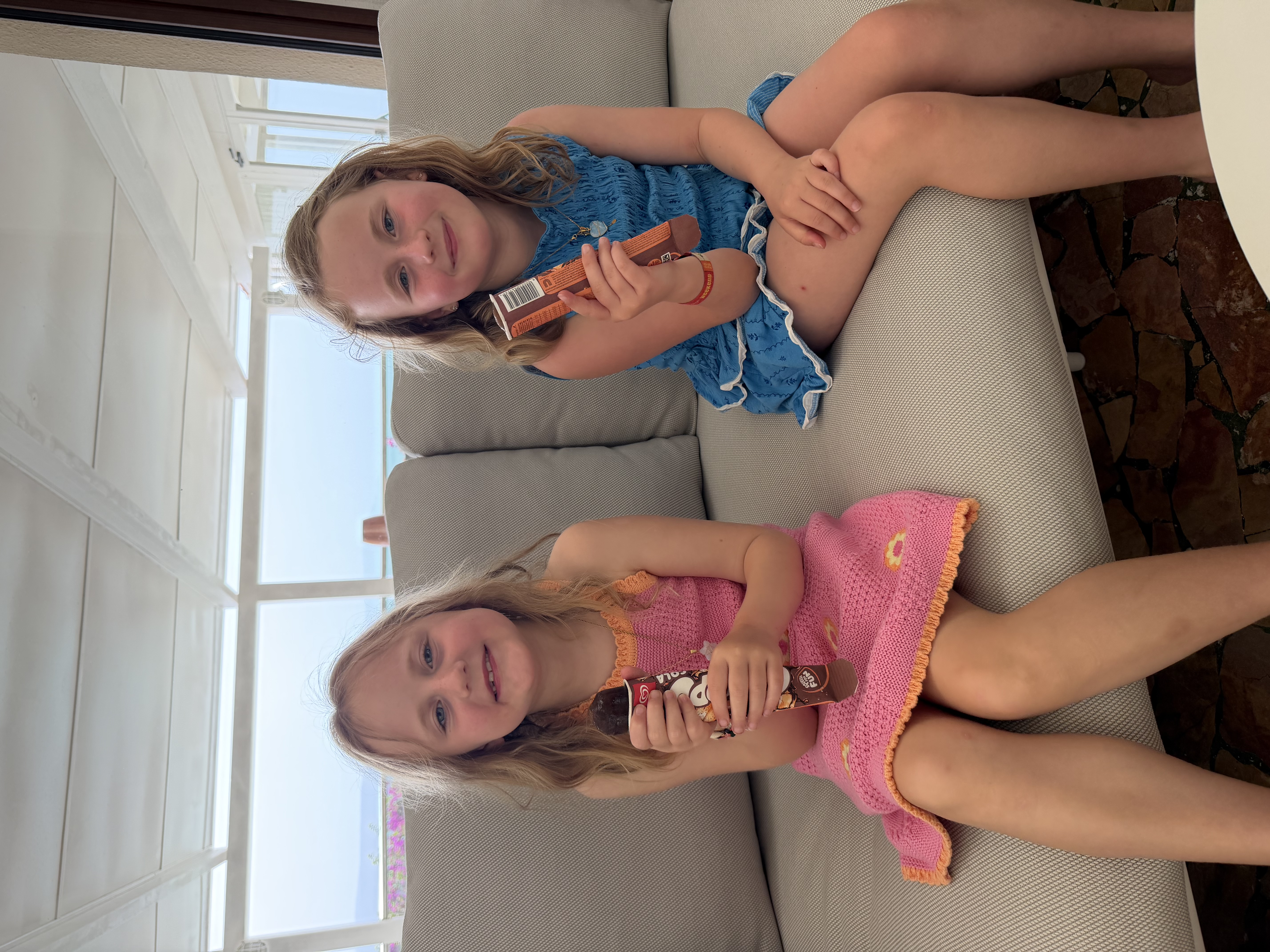 Lucia and Zoe sitting on a couch, smiling and holding ice cream treats.